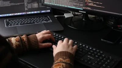 a person sitting at a desk with a laptop and a computer monitor